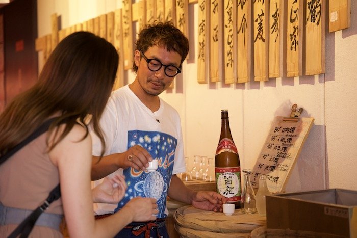 A sake sommelier offers a cup of sake to a guest at Nadagogo Sakedokoro in Kobe